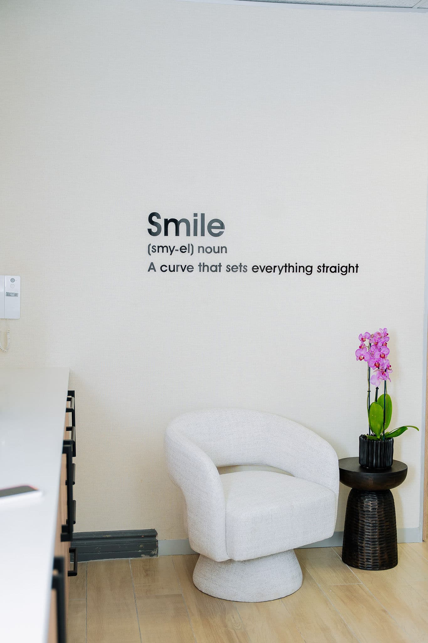 Wall lettering reading Smile: a curve that sets everything straight, beside an armchair and orchid